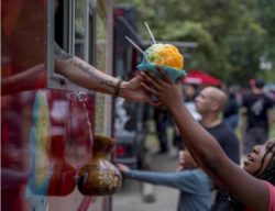 This image shows a person reaching up to receive a snow cone from a food truck vendor in southside park.