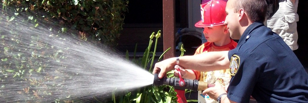 Firefighter and boy spraying water from hose